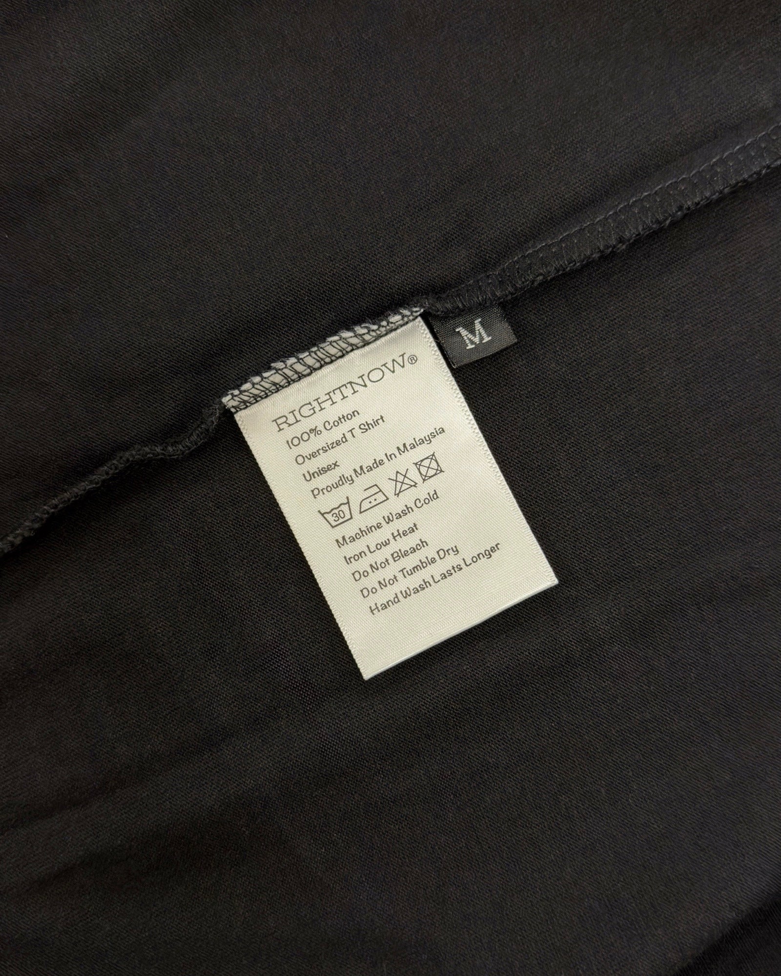 Care and composition label sewn into the side seam of a matt black Moment cotton oversized t-shirt.