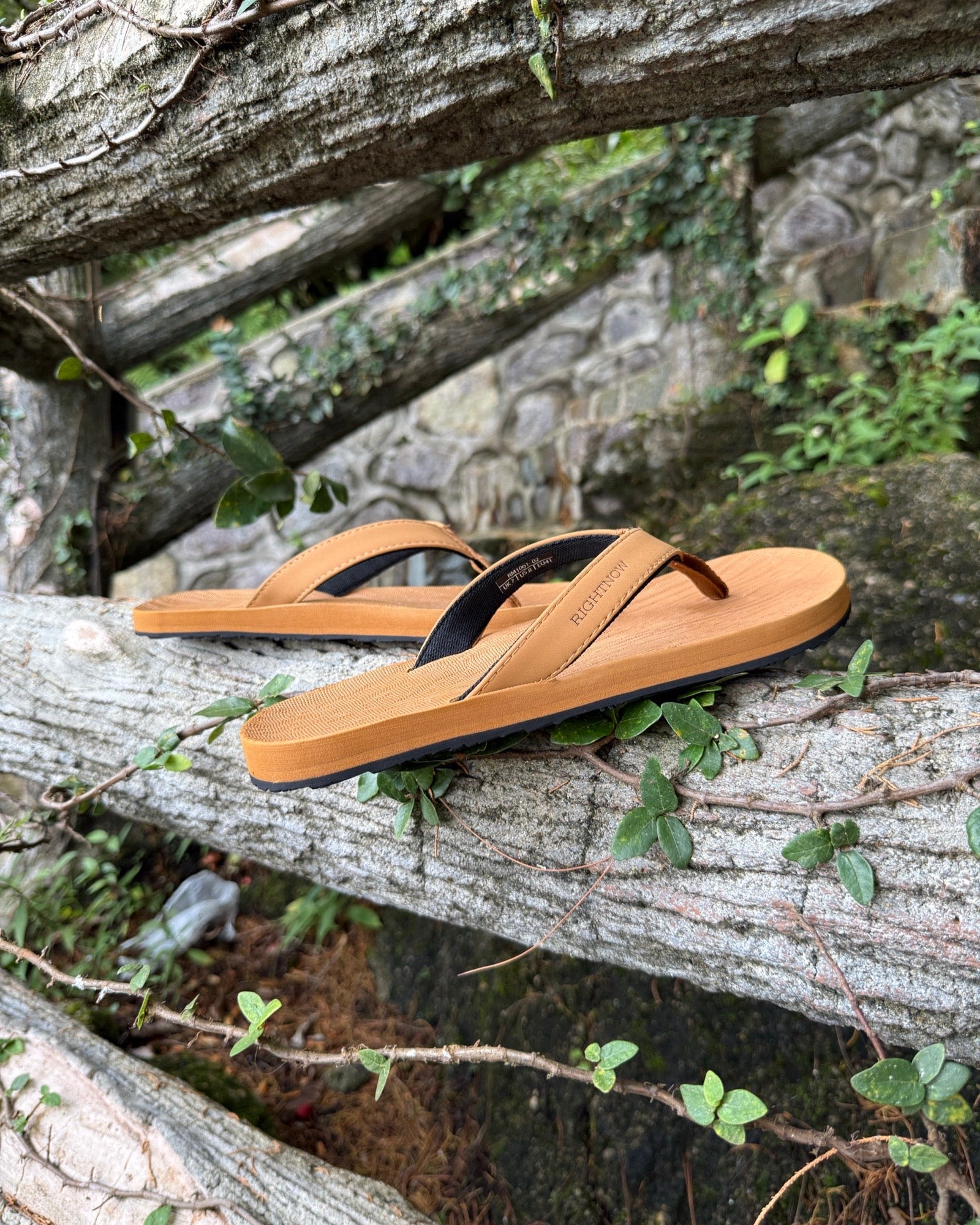 Men's earth brown Flow Thong Sandals displayed on a moss-covered fallen log amidst lush greenery, perfect for authentic moments of relaxation at a campground in nature.
