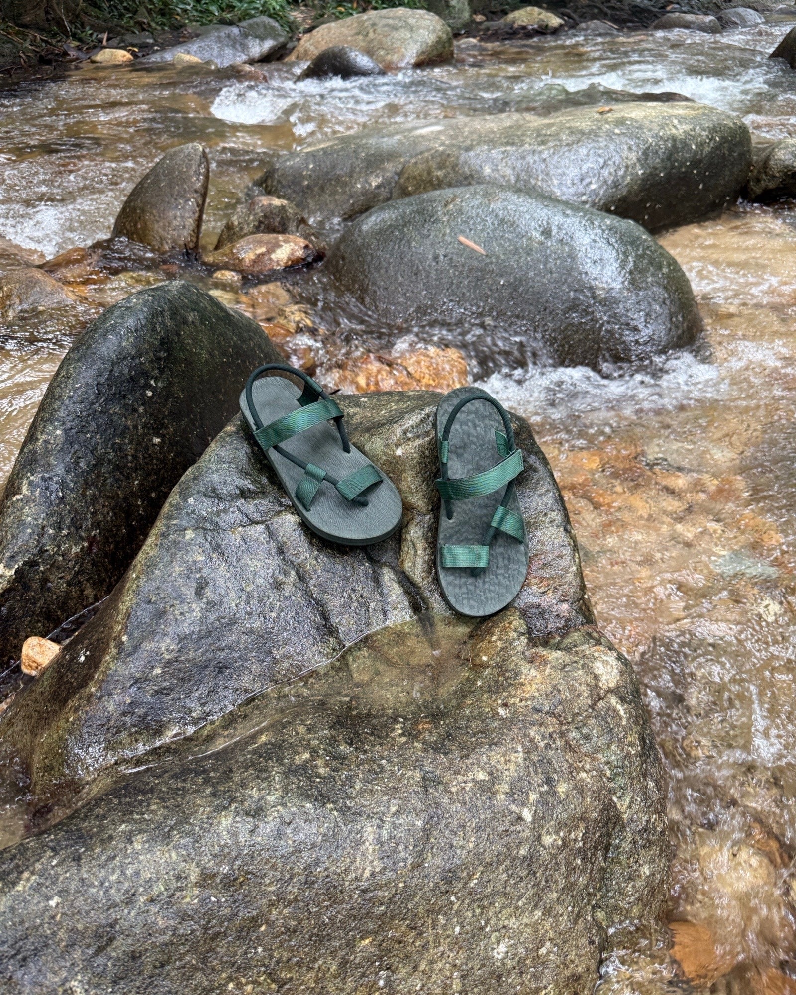 Waterproof men's natural green EXPLOre Roman Sandals on a wet boulder in a flowing jungle stream, highlighting their anti-slip soles for secure footing on any terrain.