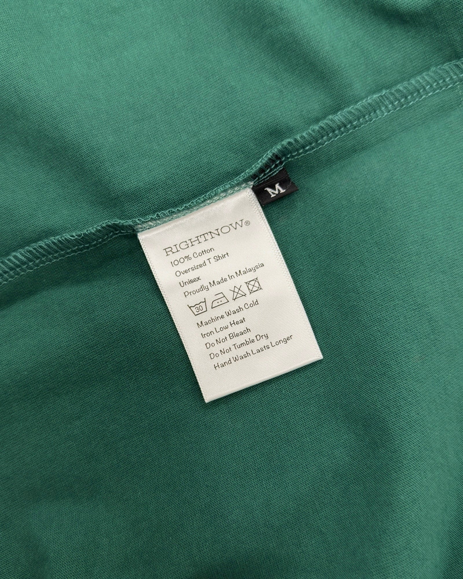 Care and composition label sewn into the side seam of a natural green Moment cotton oversized t-shirt.