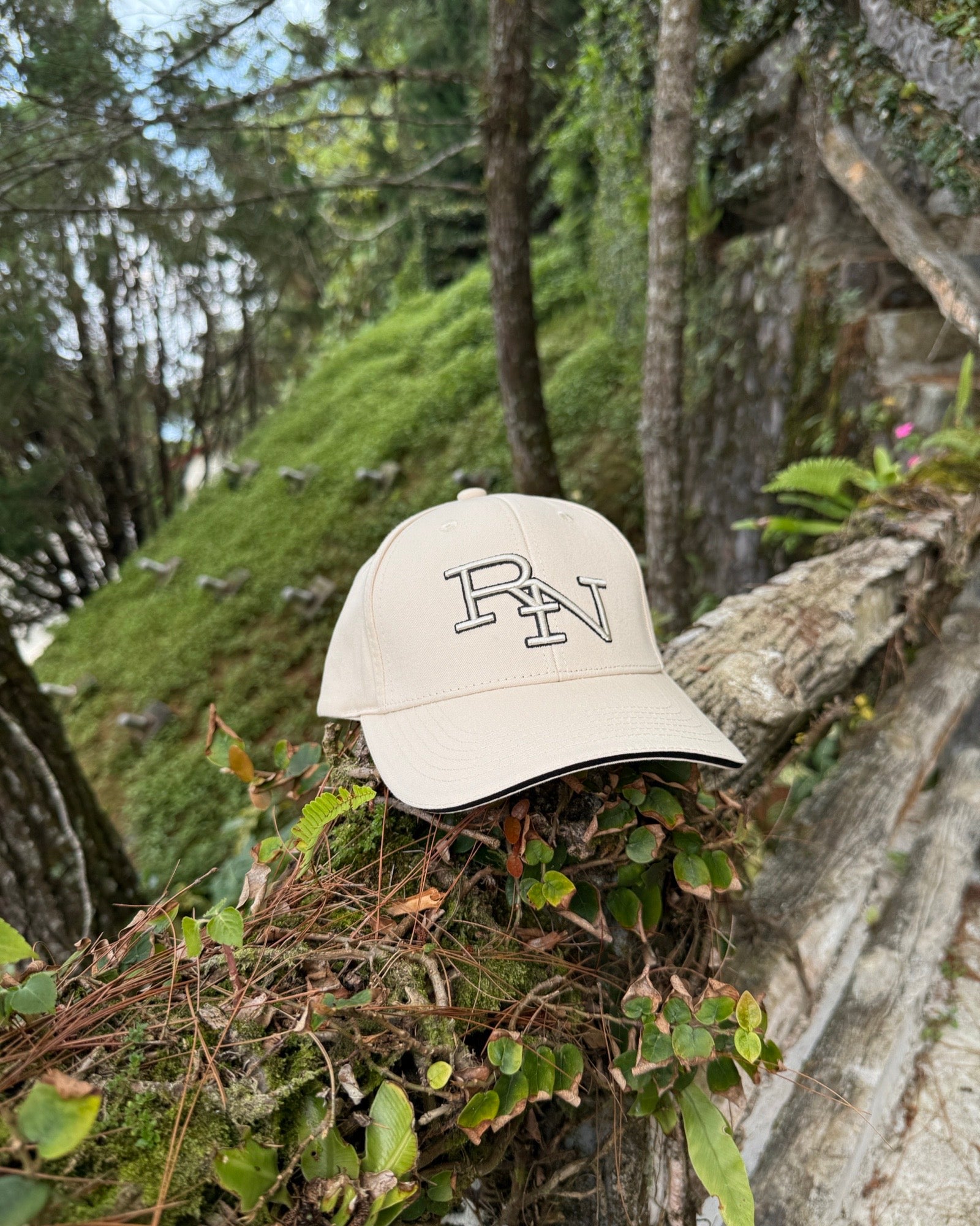 A sand beige Ignite RN logo cap placed on a mossy branch in a cool, highland forest, perfect for a simple travel and exploration lifestyle connected with nature.
