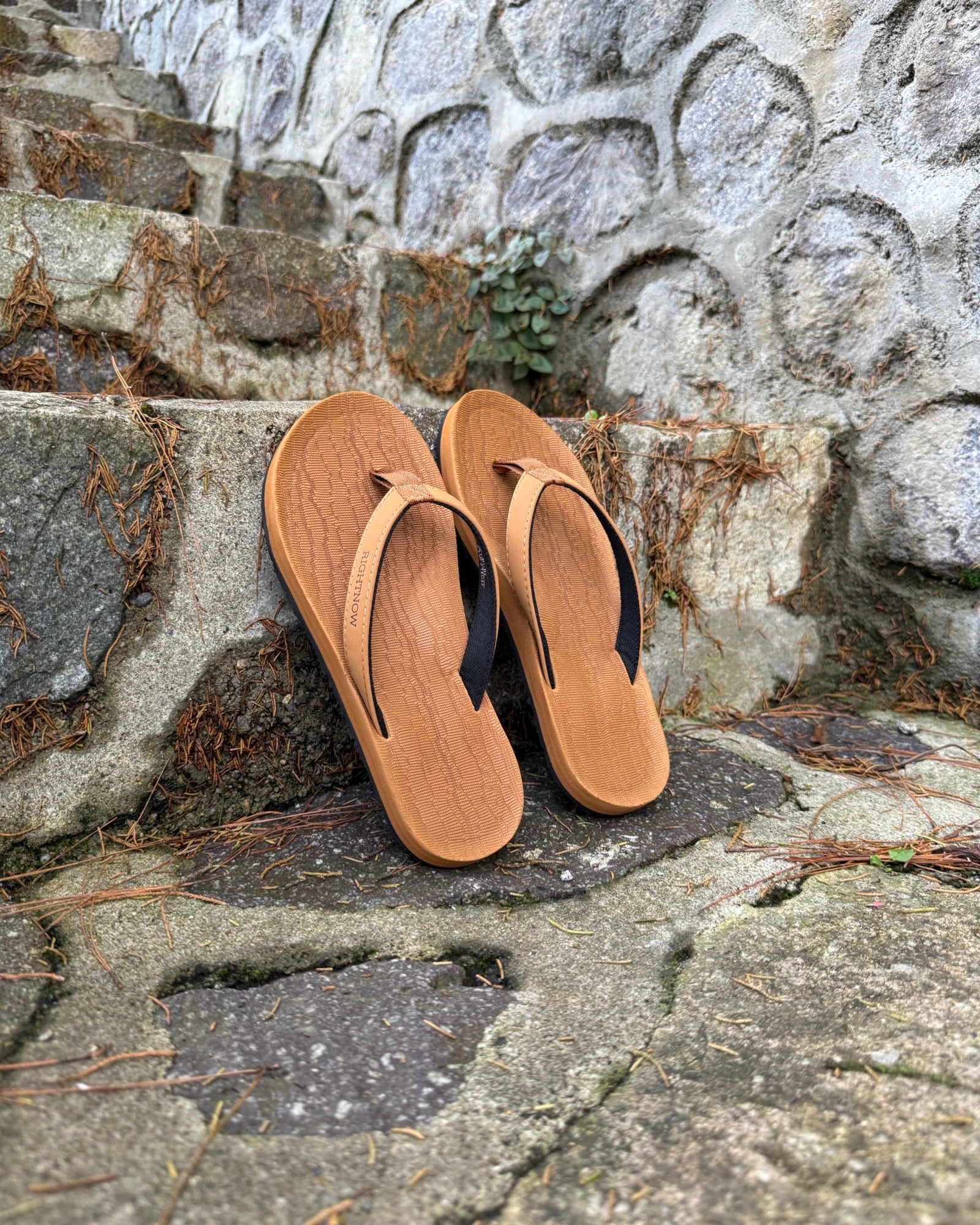 A pair of women's earth brown Flow Thong Sandals on rustic stone steps, perfect for a simple and authentic journey through historical or natural paths.