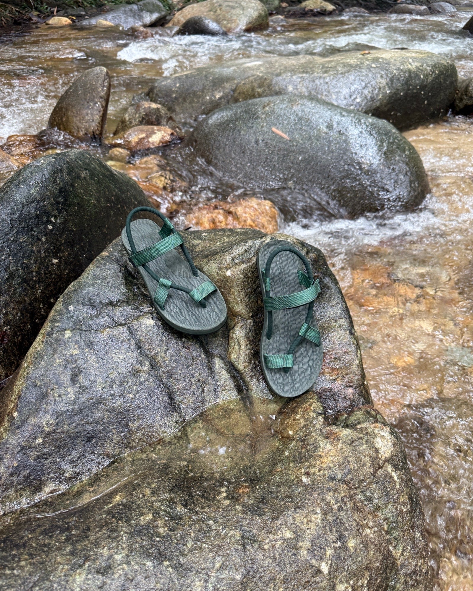 Waterproof women's natural green EXPLOre Roman Sandals on a wet boulder in a flowing jungle stream, highlighting their anti-slip soles for secure footing on any terrain.