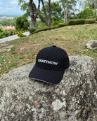 A matt black Ignite RIGHTNOW logo cap on a mountain rock at a scenic lookout point, a simple accessory for being present and enjoying an authentic view.