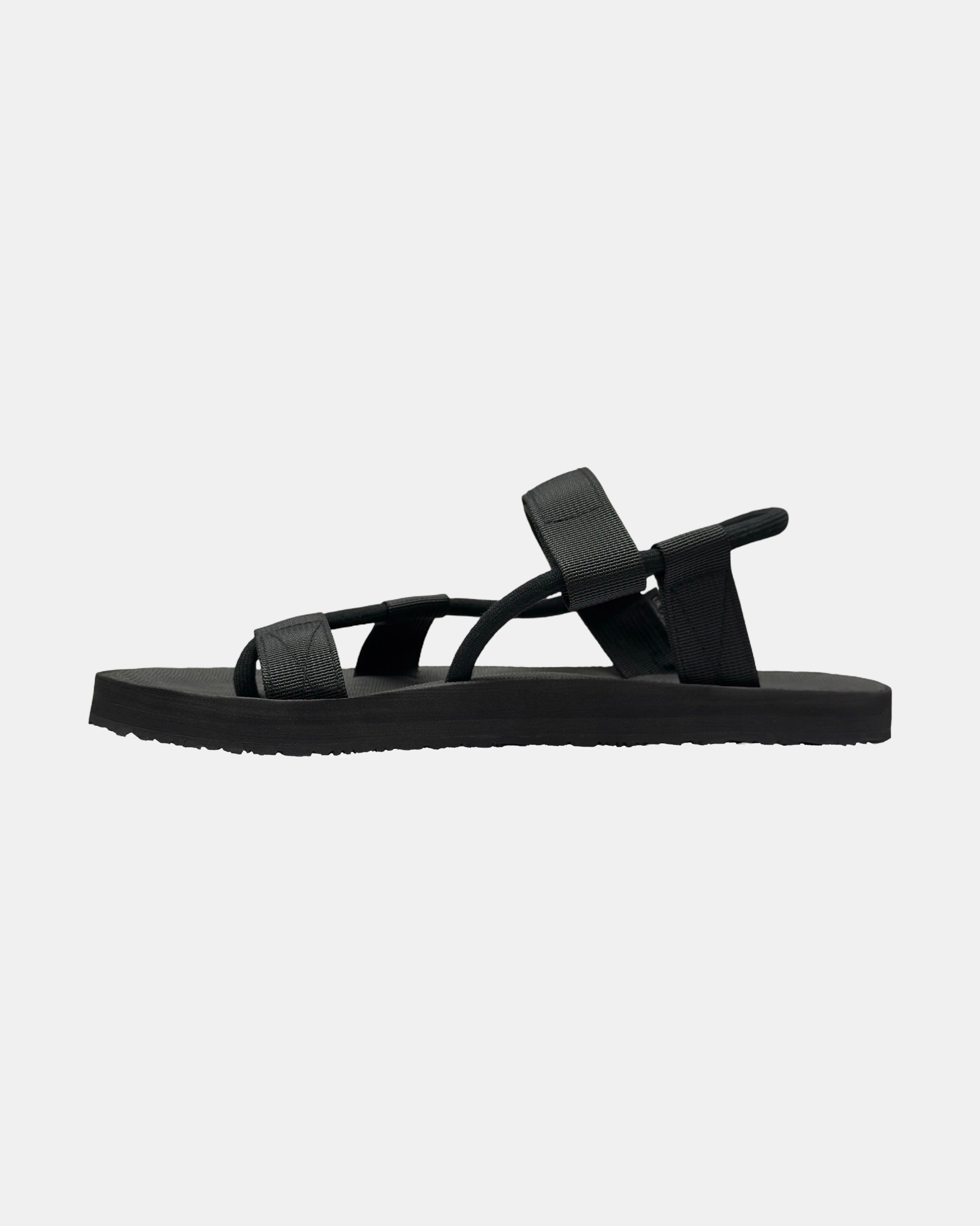 Men's matt black rubber Roman-style sandal seen from the left side, highlighting the contoured and grooved topsole with embedded arch support.