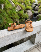 Men's earth brown EXPLOre Roman Sandals on a bridge over a serene waterfall and lush greenery, perfect for travel and finding a quiet moment of presence in nature.