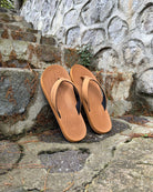 A pair of men's earth brown Flow Thong Sandals on rustic stone steps, perfect for a simple and authentic journey through historical or natural paths.