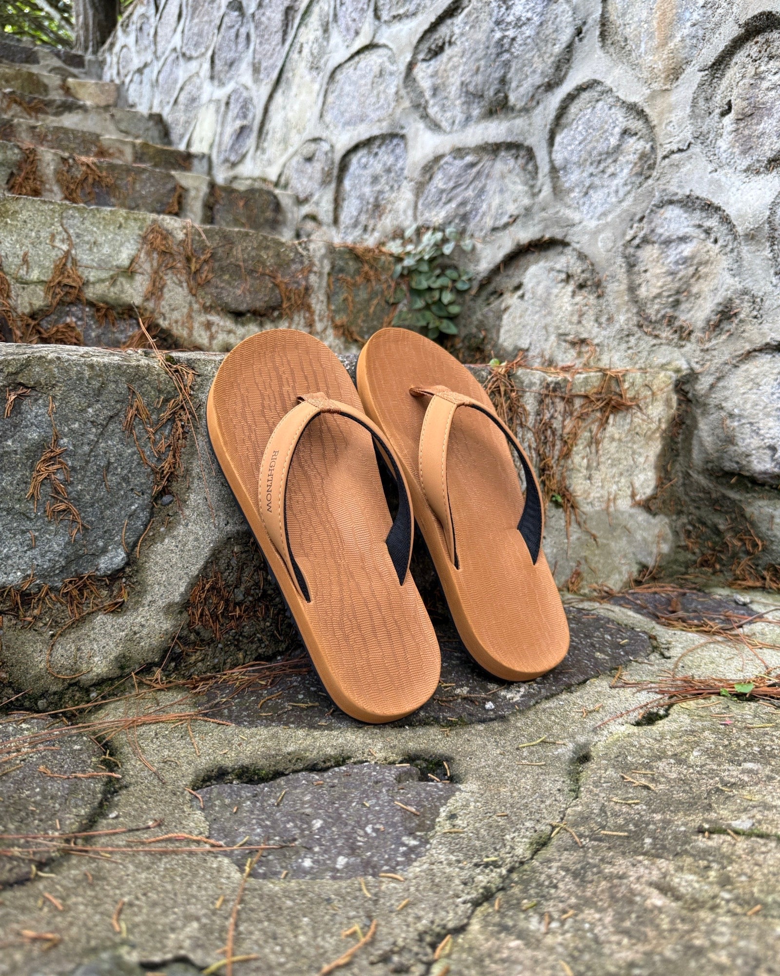 A pair of men's earth brown Flow Thong Sandals on rustic stone steps, perfect for a simple and authentic journey through historical or natural paths.