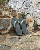 A pair of men's natural green Flow Thong Sandals on rustic stone steps, perfect for a simple and authentic journey through historical or natural paths.
