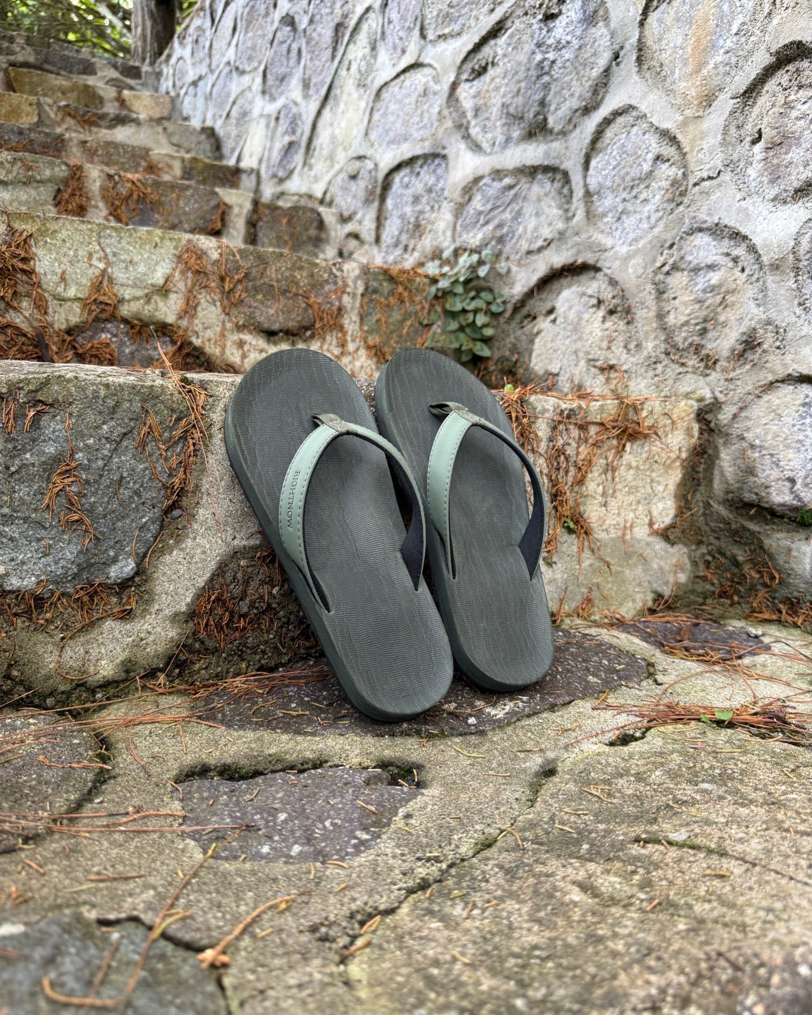A pair of men's natural green Flow Thong Sandals on rustic stone steps, perfect for a simple and authentic journey through historical or natural paths.