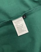 Care and composition label sewn into the side seam of a natural green Moment cotton oversized t-shirt.