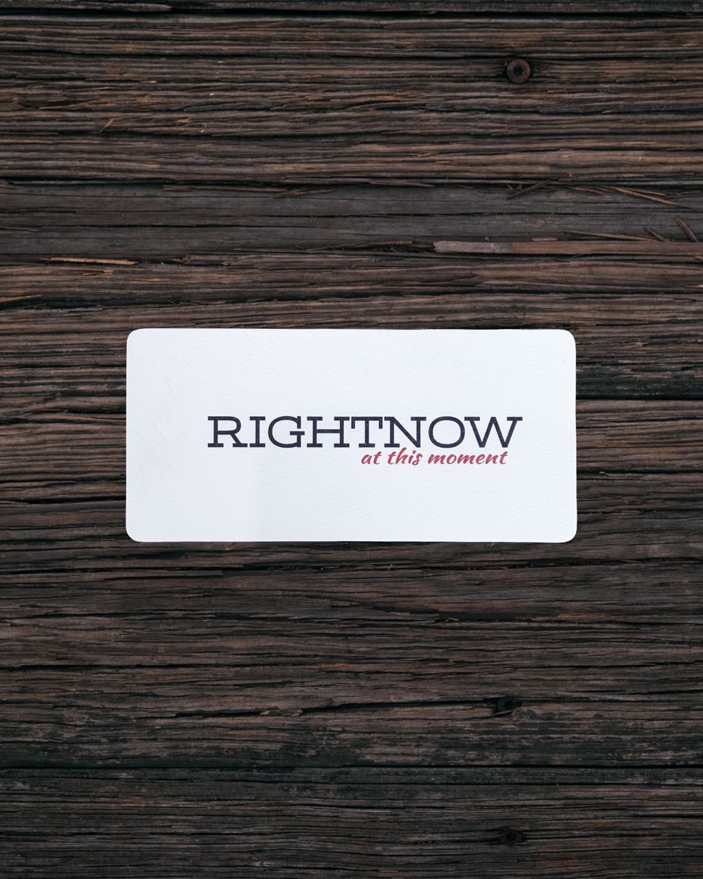 White card with 'RIGHTNOW' name and tagline 'at this moment' on a wooden surface.