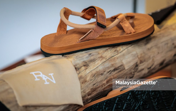 Brown EXPLOre roman sandal on a wooden log with RN branding visible.