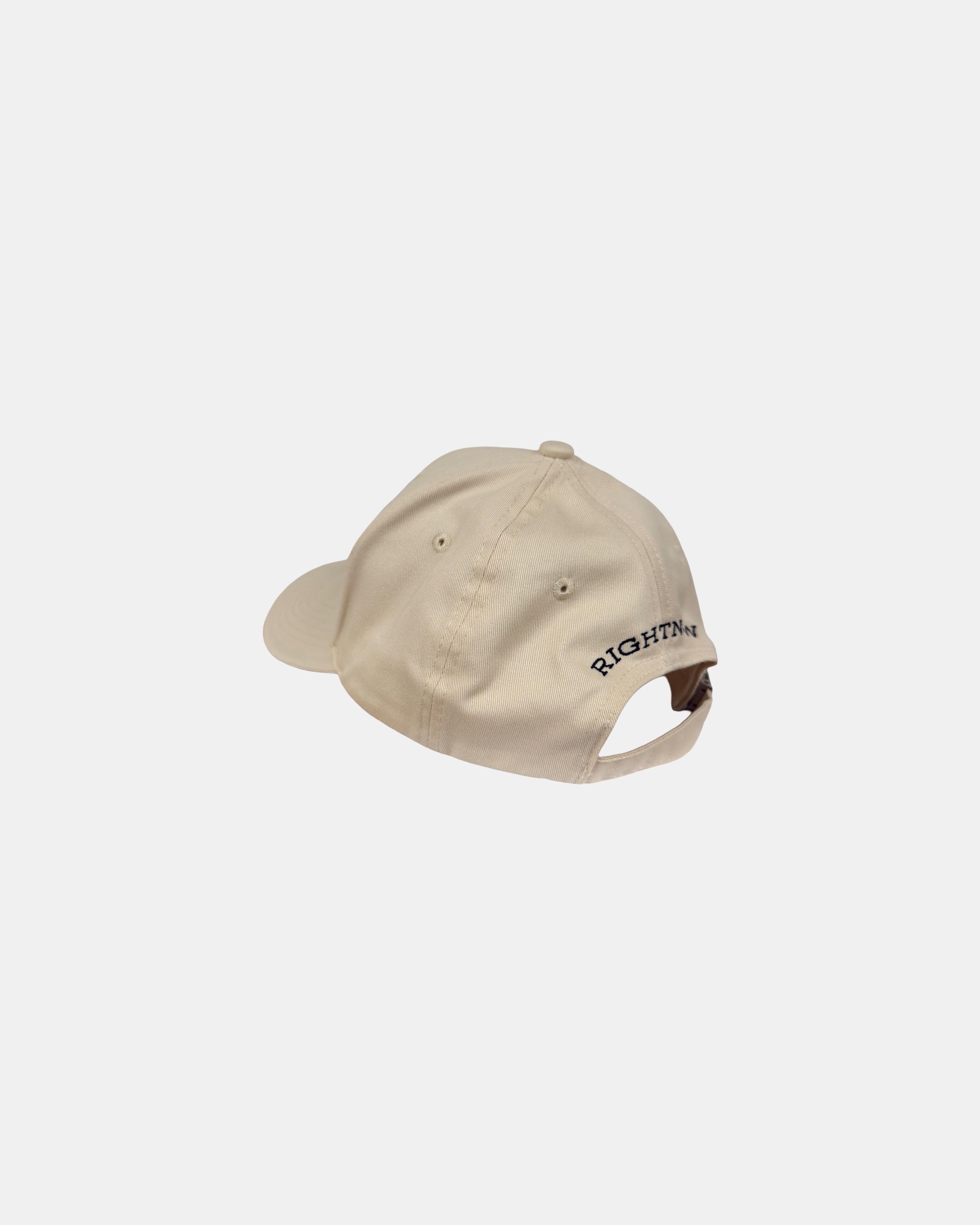 Angled 45-degree back-left view of a sand beige Ignite cap, featuring 'RIGHTNOW' embroidery in black above the adjustable strap, showcasing inspiring presence.