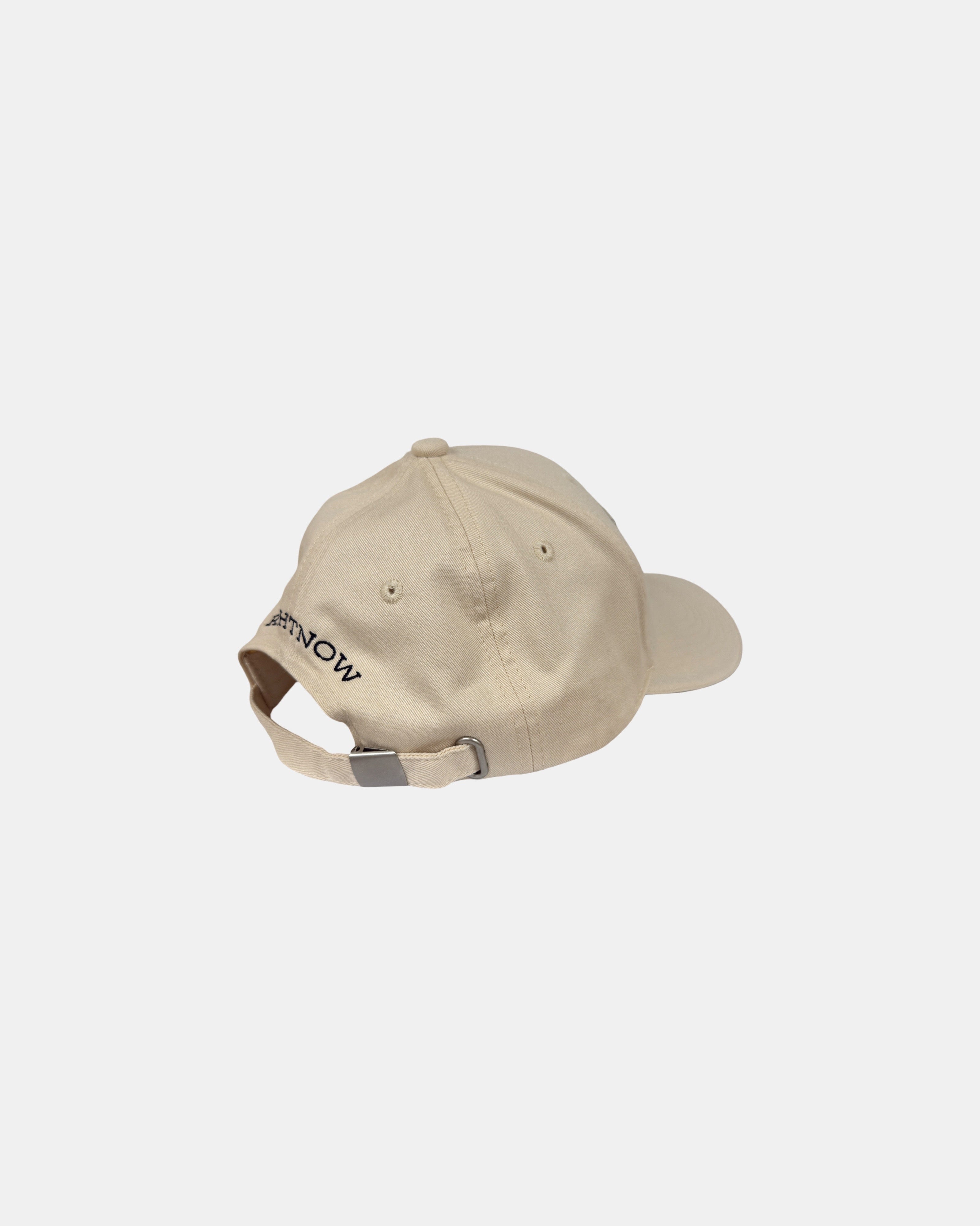 Angled 45-degree back-right view of a sand beige Ignite cap with 'RIGHTNOW' embroidered in black, highlighting the brand's core value of being present.
