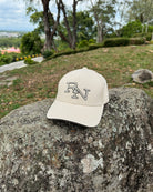 A sand beige Ignite RN logo cap on a mountain rock at a scenic lookout point, a simple accessory for being present and enjoying an authentic view.