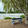 A simple blue bench under a leafy tree overlooking a calm lake, offering a tranquil spot for quiet contemplation and being present.