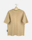 The back view of a unisex Moment oversized plain t-shirt in sand beige, showing the clean design and drape of the premium cotton fabric on a hanger.