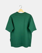 The back view of a unisex Moment oversized plain t-shirt in natural green, showing the clean design and drape of the premium cotton fabric on a hanger.