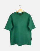 Unisex Moment oversized plain t-shirt in natural green, made from premium cotton, shown from the front to feature its butterfly-knitted crewneck collar on a hanger.