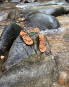Waterproof women's earth brown EXPLOre Roman Sandals on a wet boulder in a flowing jungle stream, highlighting their anti-slip soles for secure footing on any terrain.