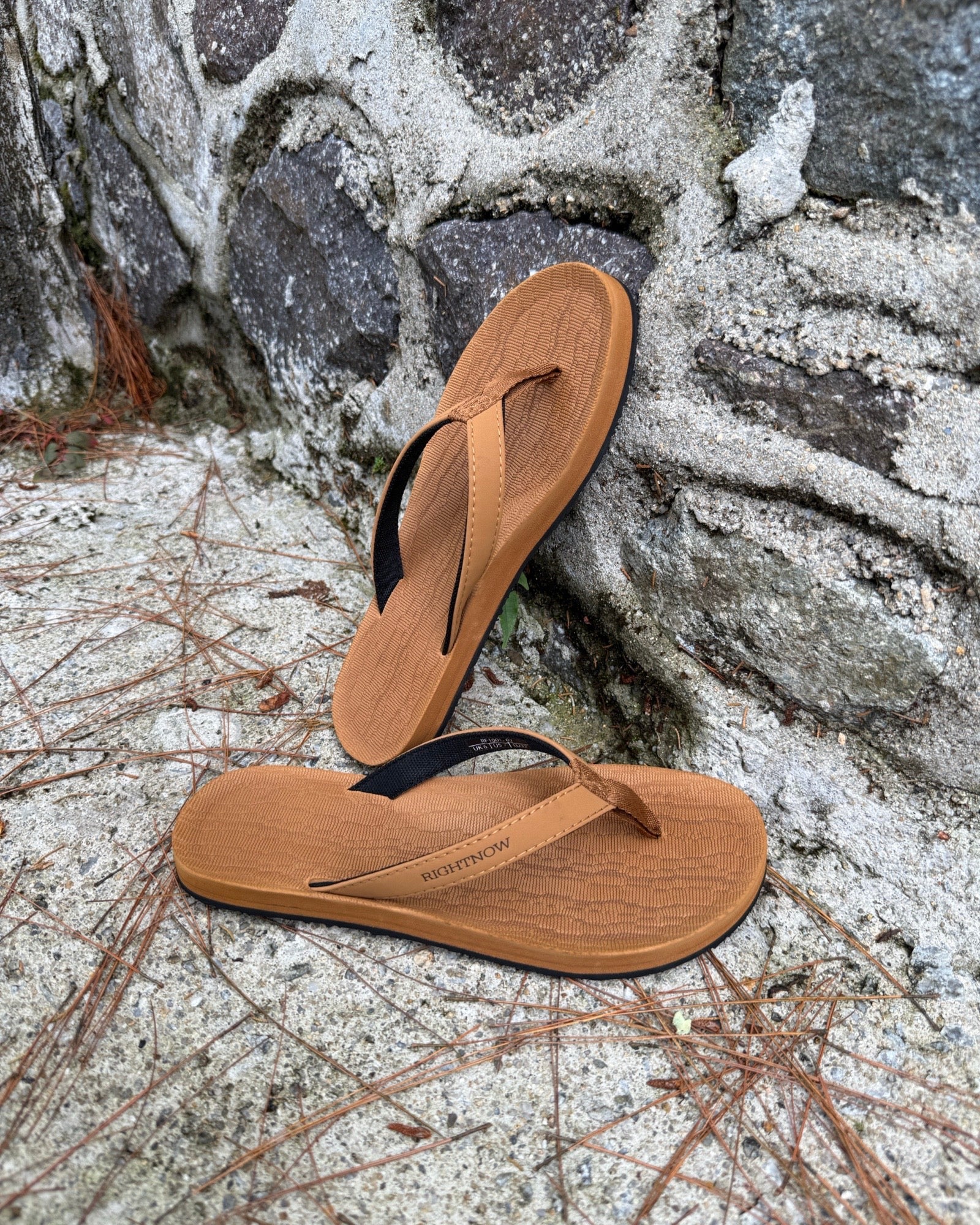 Women's earth brown Flow Thong Sandals leaning against a textured stone wall, conveying a casual yet authentic style ready for everyday adventures.