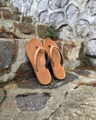 A pair of women's earth brown Flow Thong Sandals on rustic stone steps, perfect for a simple and authentic journey through historical or natural paths.