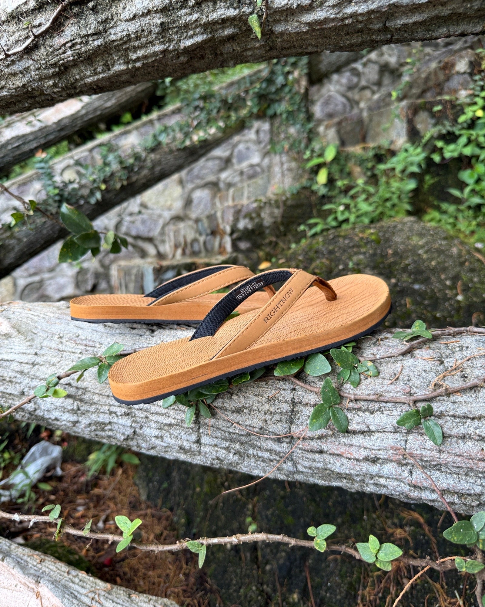 Women's earth brown Flow Thong Sandals displayed on a moss-covered fallen log amidst lush greenery, perfect for authentic moments of relaxation at a campground in nature.