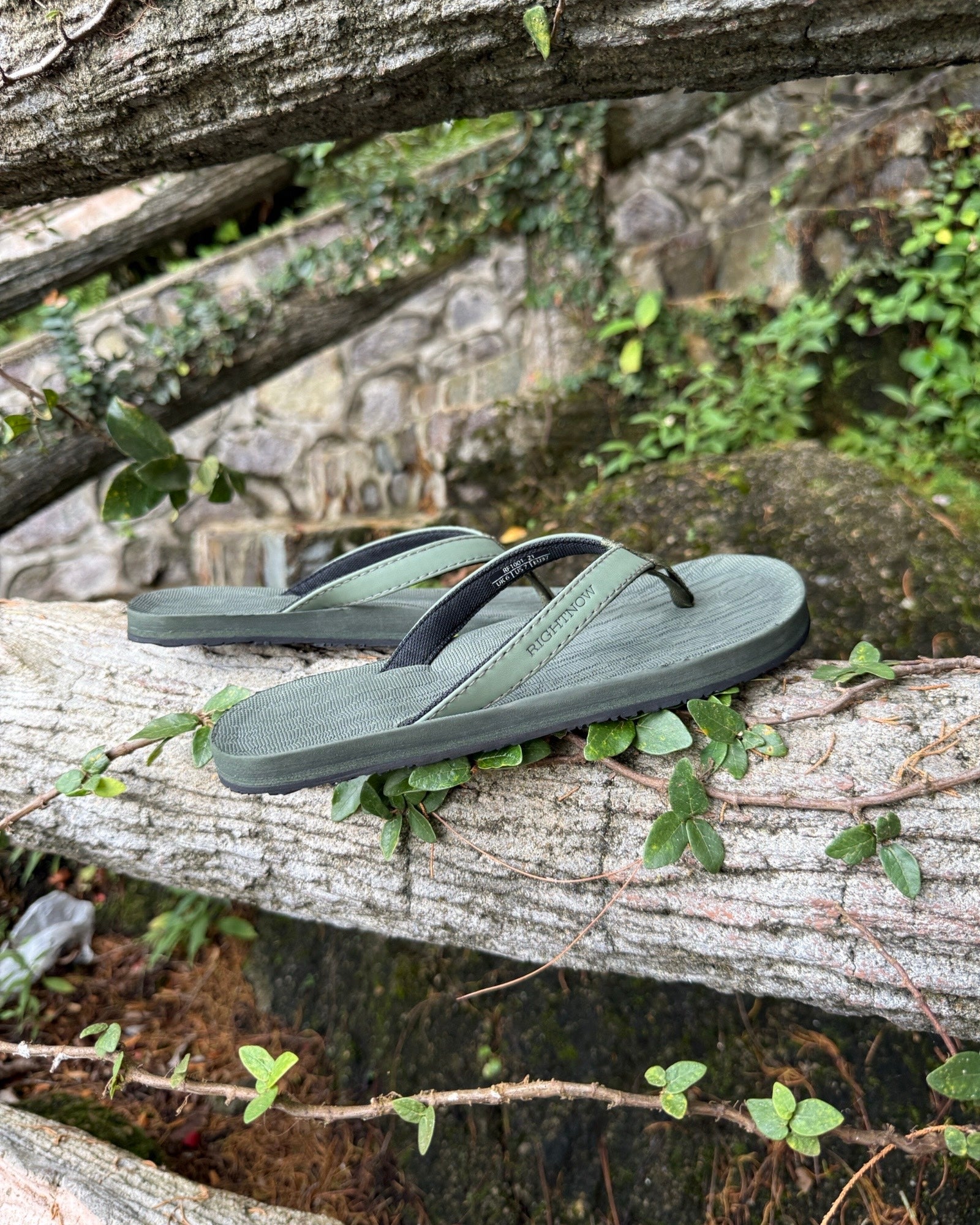 Women's natural green Flow Thong Sandals displayed on a moss-covered fallen log amidst lush greenery, perfect for authentic moments of relaxation at a campground in nature.